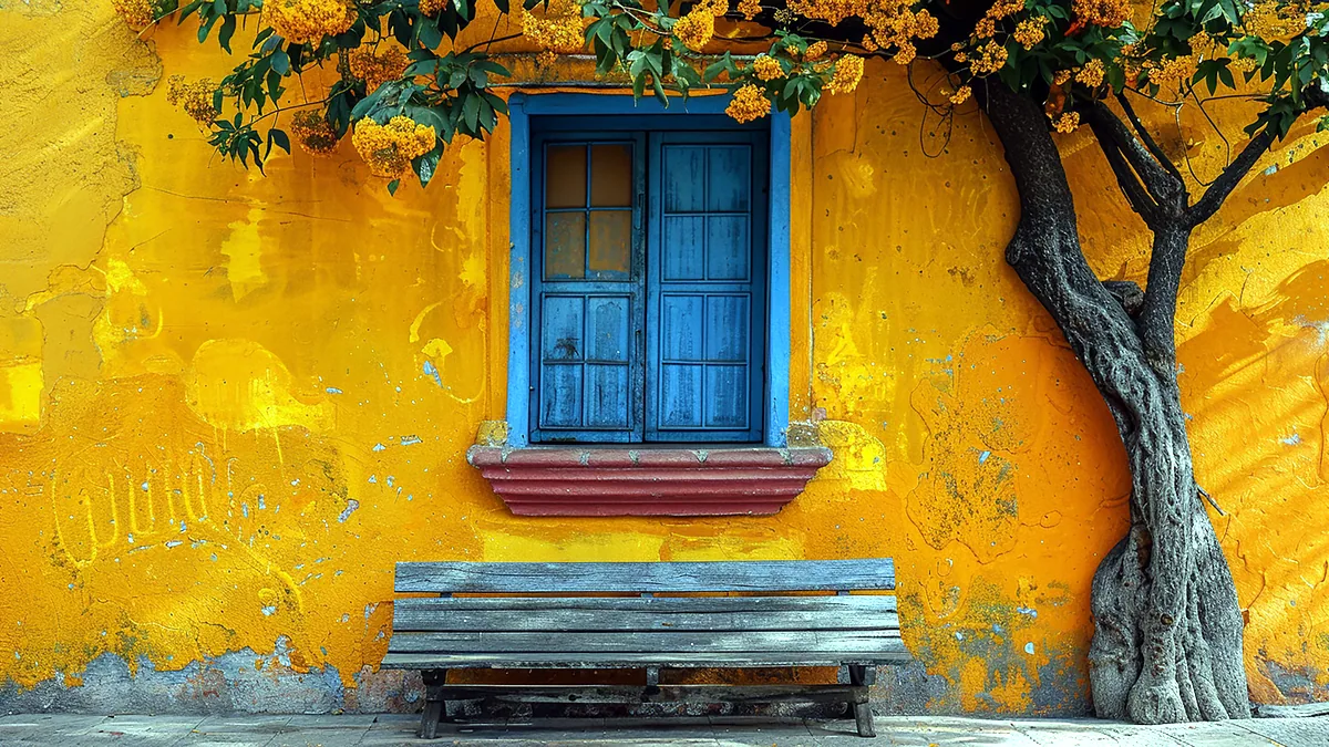 Calle empedrada de una casa colonial con balcones de madera y flores, en la luz amable de la manana.