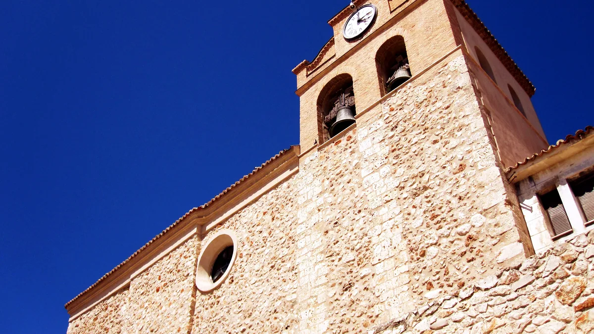 Fachada de una iglesia canaria bajo el sol de la tarde, con su campanario y las ventanas de madera pintadas.
