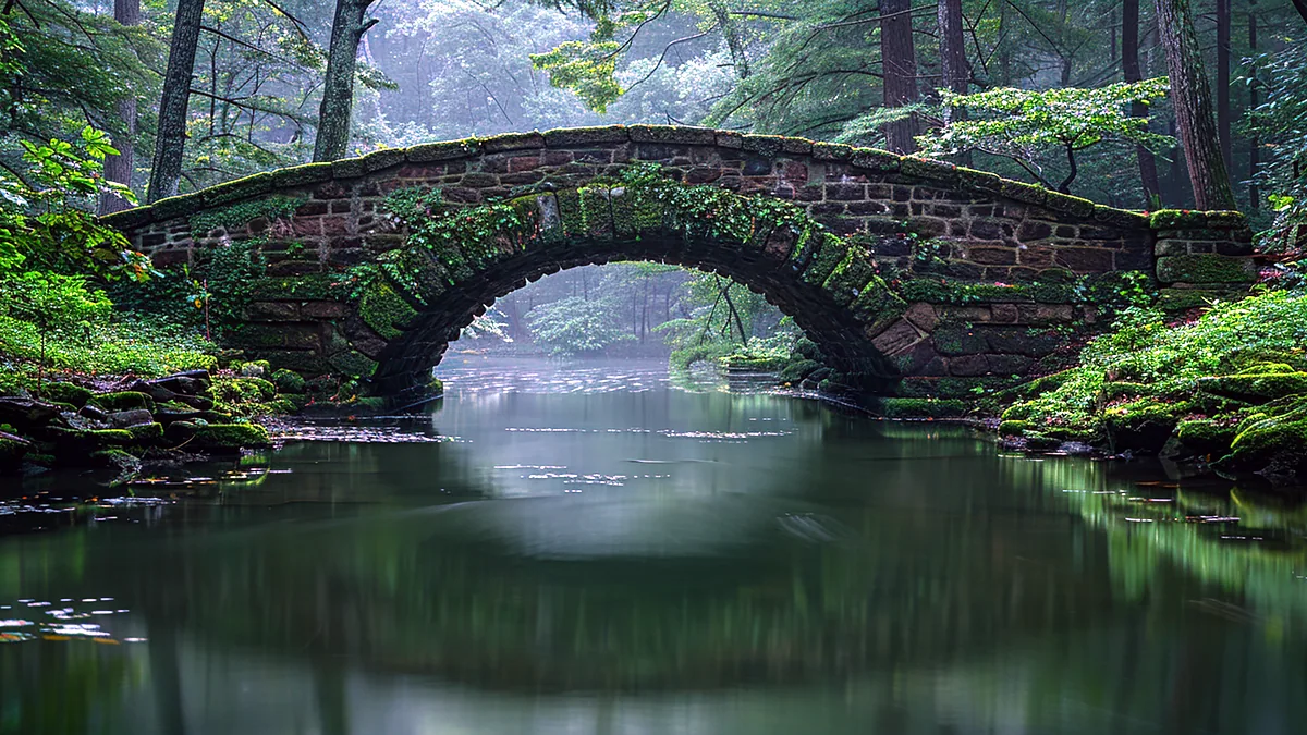 Puente de piedra sobre un rio verde en el campo ingles, con el musgo en las rocas y la niebla al fondo.