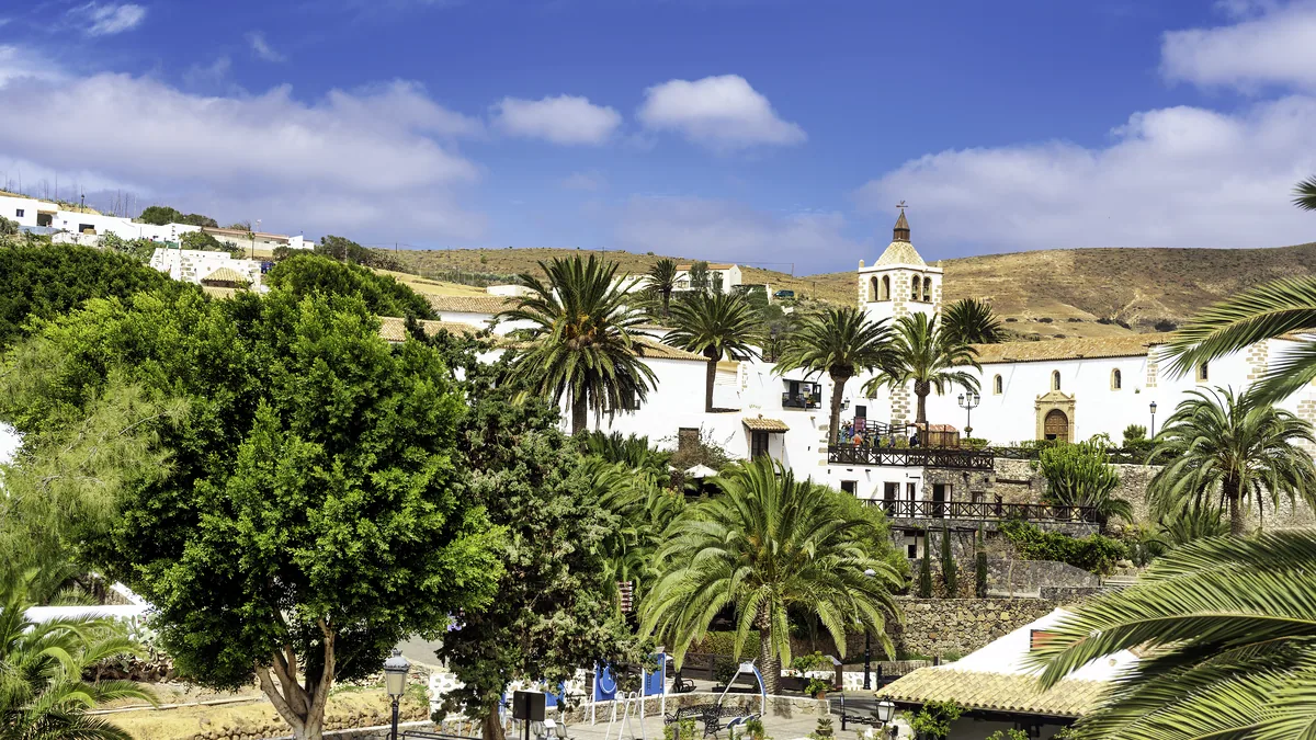Casa de piedra con muros de cal blanca y un porton de madera, encajada en el barranco.